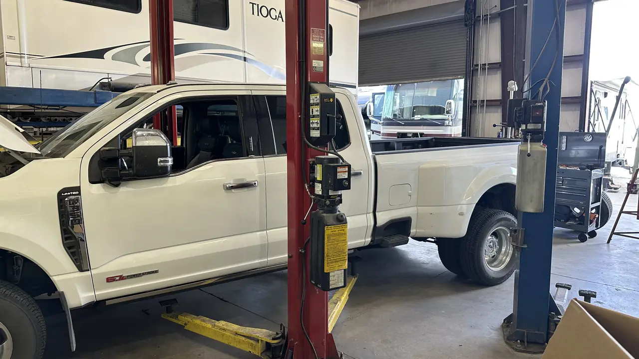 A dual rear wheel pickup raised in one bay with a Class C motorhome in the next bay